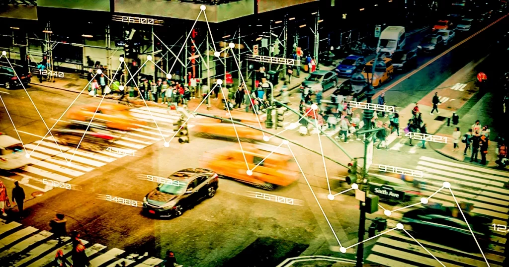 Um cruzamento urbano com diversas pessoas e veículos, com pontos de ligação, representando a capa do artigo "Roteirização Inteligente: Como Reduzir Custos e Melhorar a Entrega com Apoio da Tecnologia"